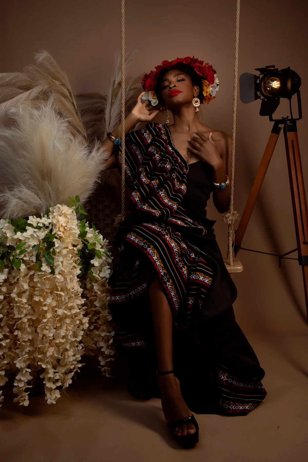 Model in a striped dress and a floral crown, seated on a swing in the studio.
