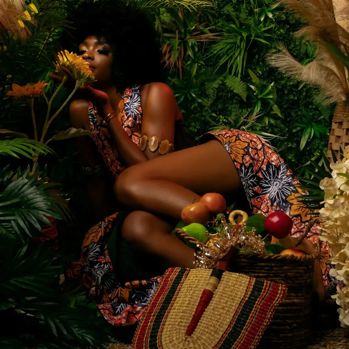 Model in a patterned wrap dress among tropical leaves and fruit.